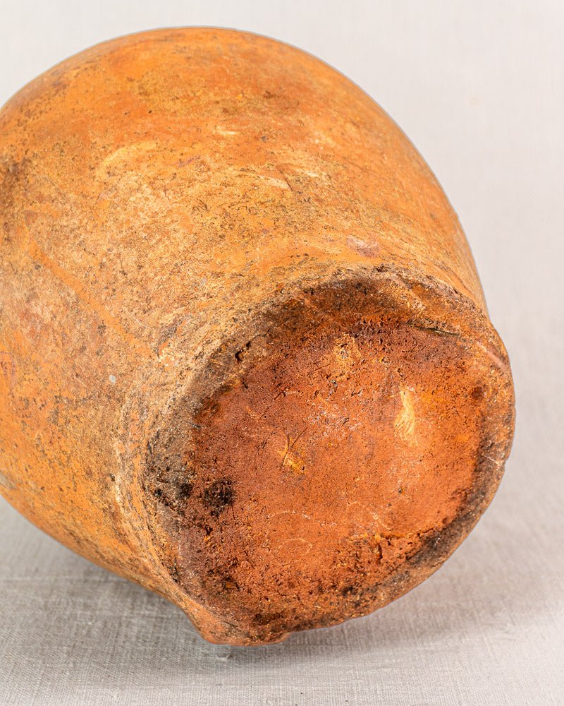 Antique French glazed terracotta vinaigrier, rounded weathered base, warm orange-brown on light gray surface.