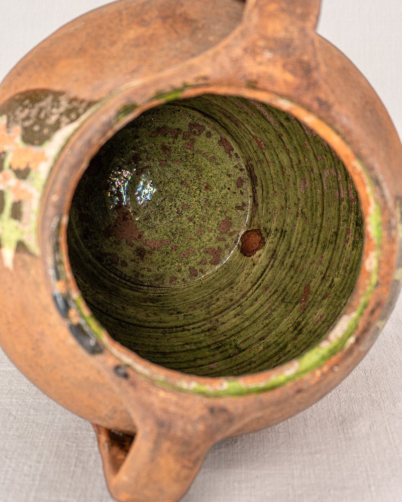 Antique French glazed terracotta vinaigrier with green mottled interior and worn brown-green exterior.
