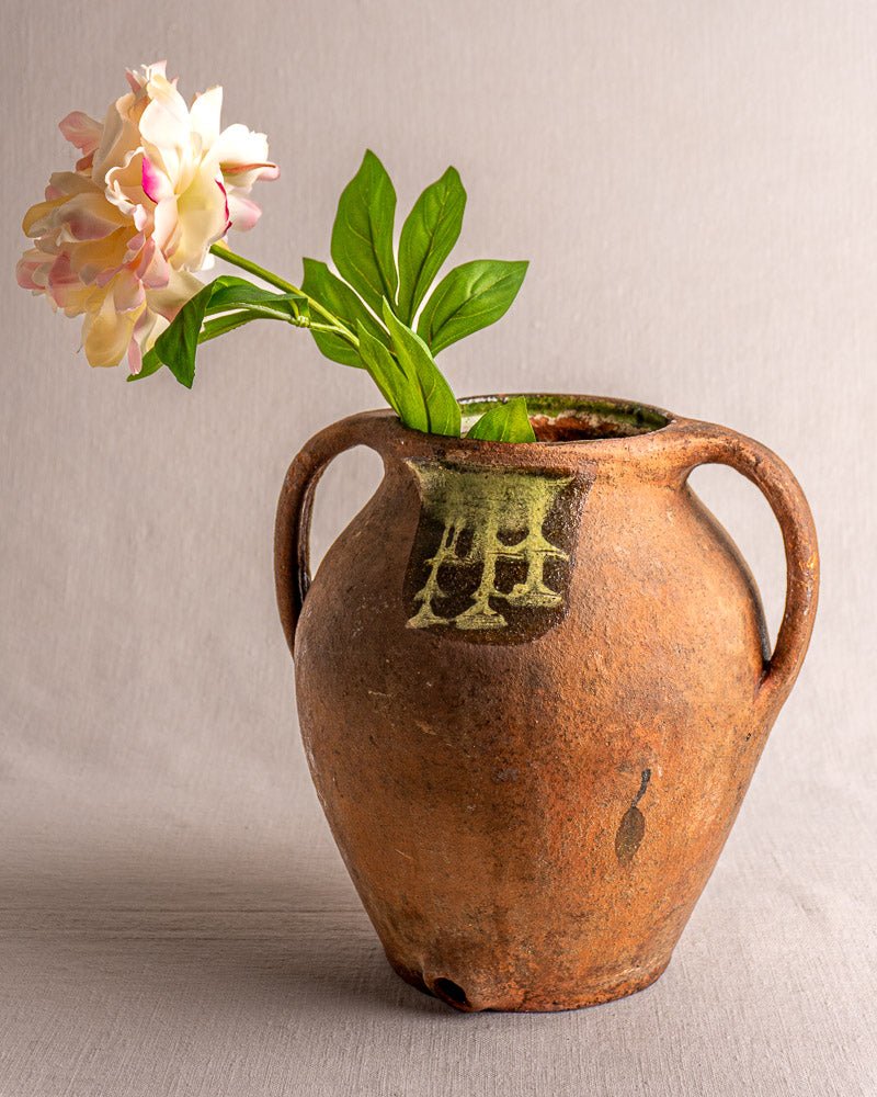 Antique French brown glazed terracotta vinaigrier with green accents, holding a pink flower.