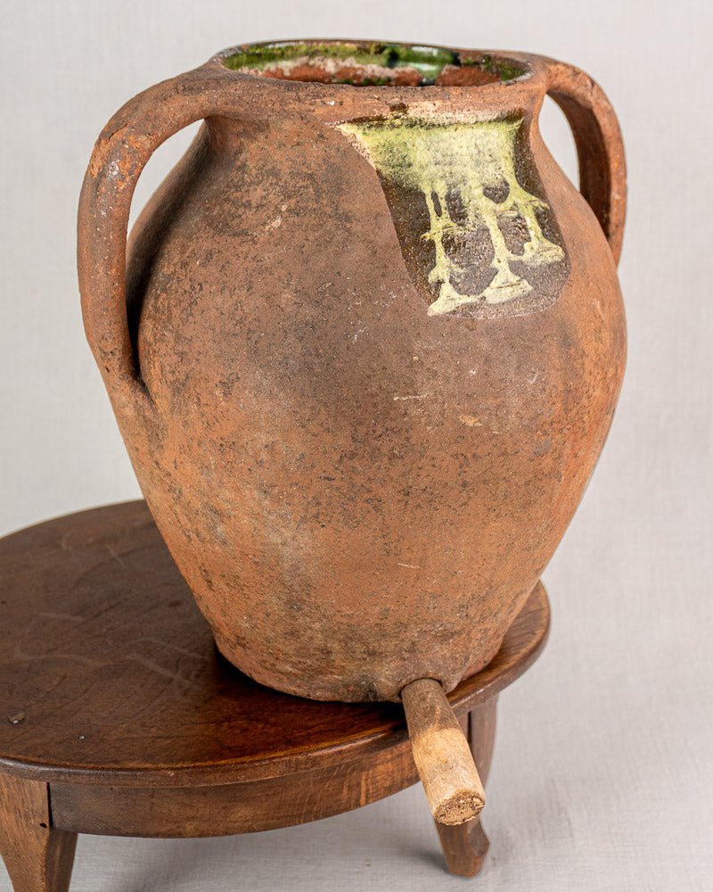 Antique French glazed terracotta vinaigrier with side handles, green glaze patch, aged surface.