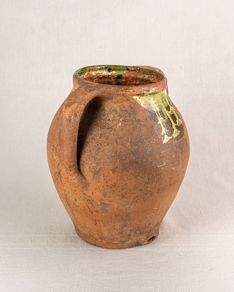 Large antique French terracotta vinaigrier with green glaze detail and chipped rim on fabric background.