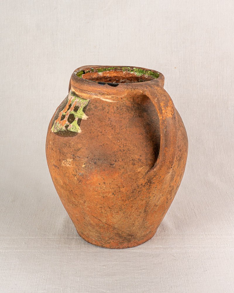Antique French glazed terracotta vinaigrier with rustic brown finish, single handle, green and white detail.