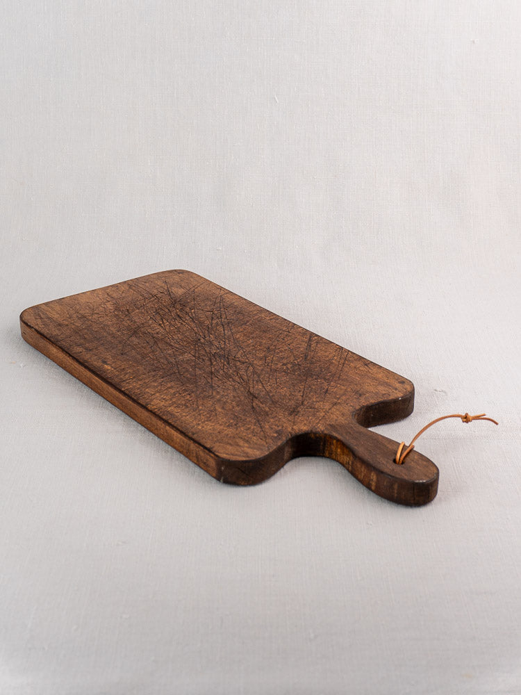 Antique French cutting board with paddle handle and twine loop, late 19th century, on light fabric.