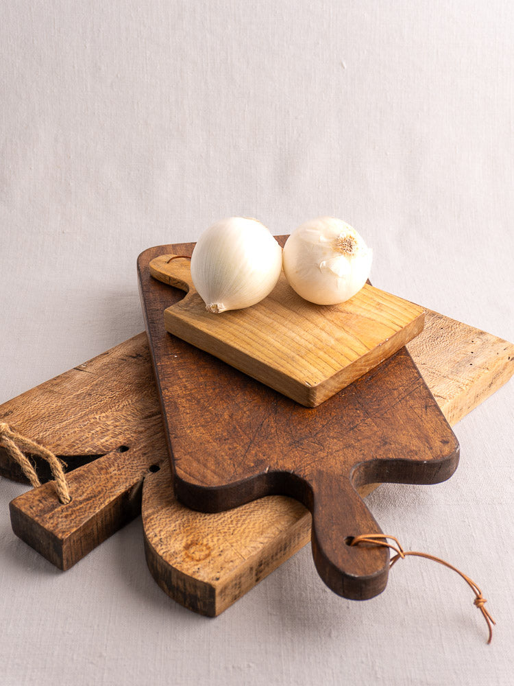 Antique French cutting boards with paddle handles, small planche à découper, white onions, neutral background.