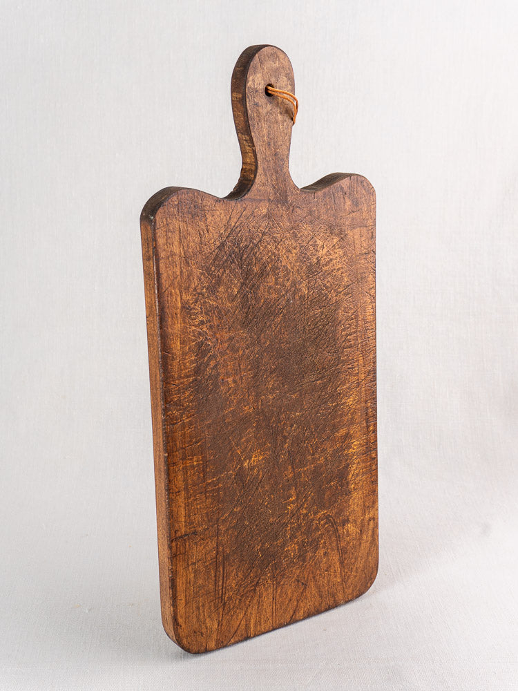 Antique French cutting board with paddle handle, late 19th century, worn surface and leather loop, rustic farmhouse decor.