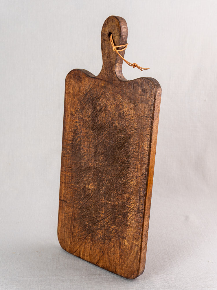 Antique French cutting board with paddle handle, late 19th century, worn finish and knife marks, upright on light grey surface.