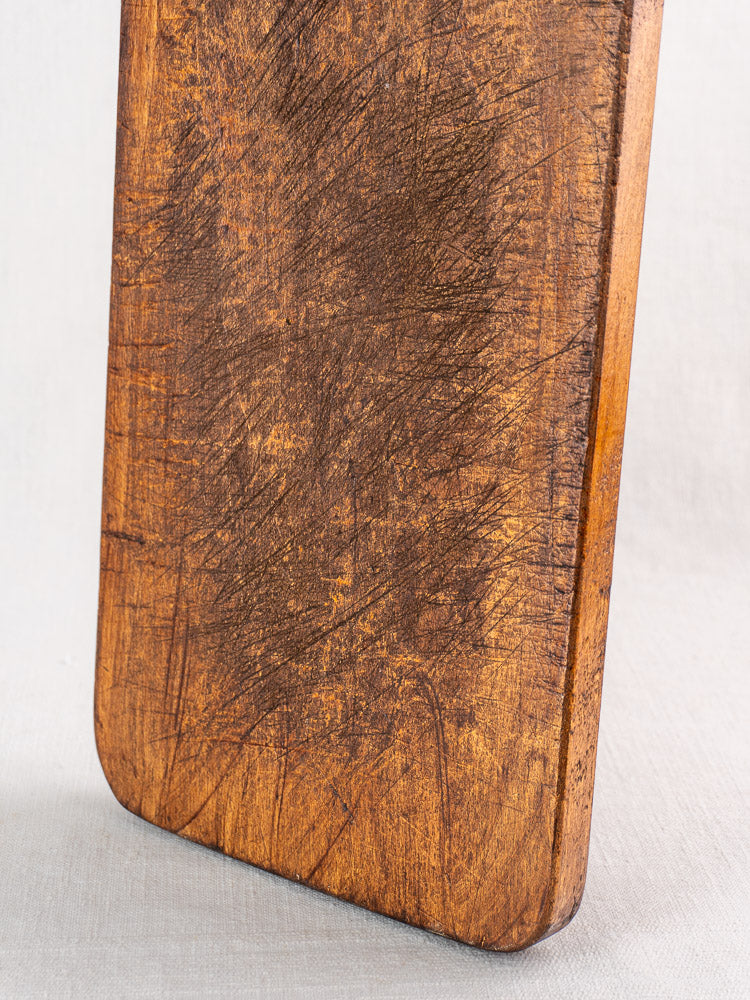 Antique French cutting board with paddle handle and aged marks, late 19th century, on light surface.