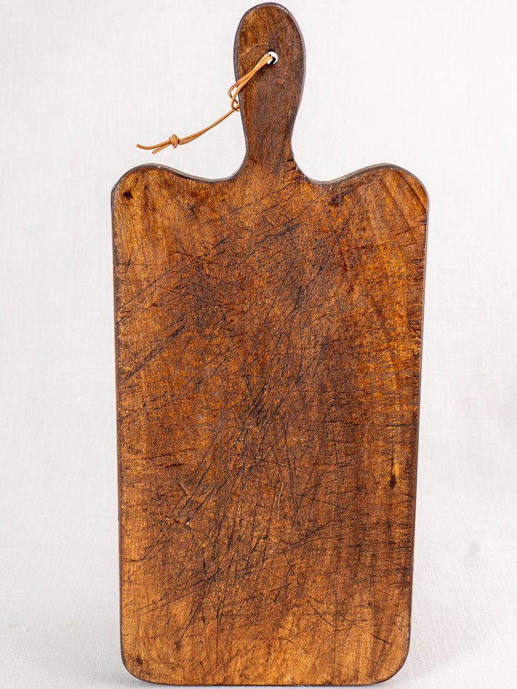Antique French cutting board with paddle handle, late 19th century, visible knife marks, on a light surface.