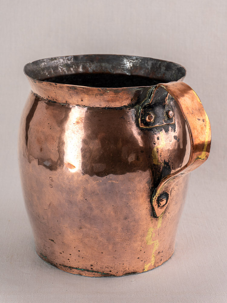Antique French hammered copper pitcher with large handle, late 18th century, showing dents and rich patina on a neutral surface.
