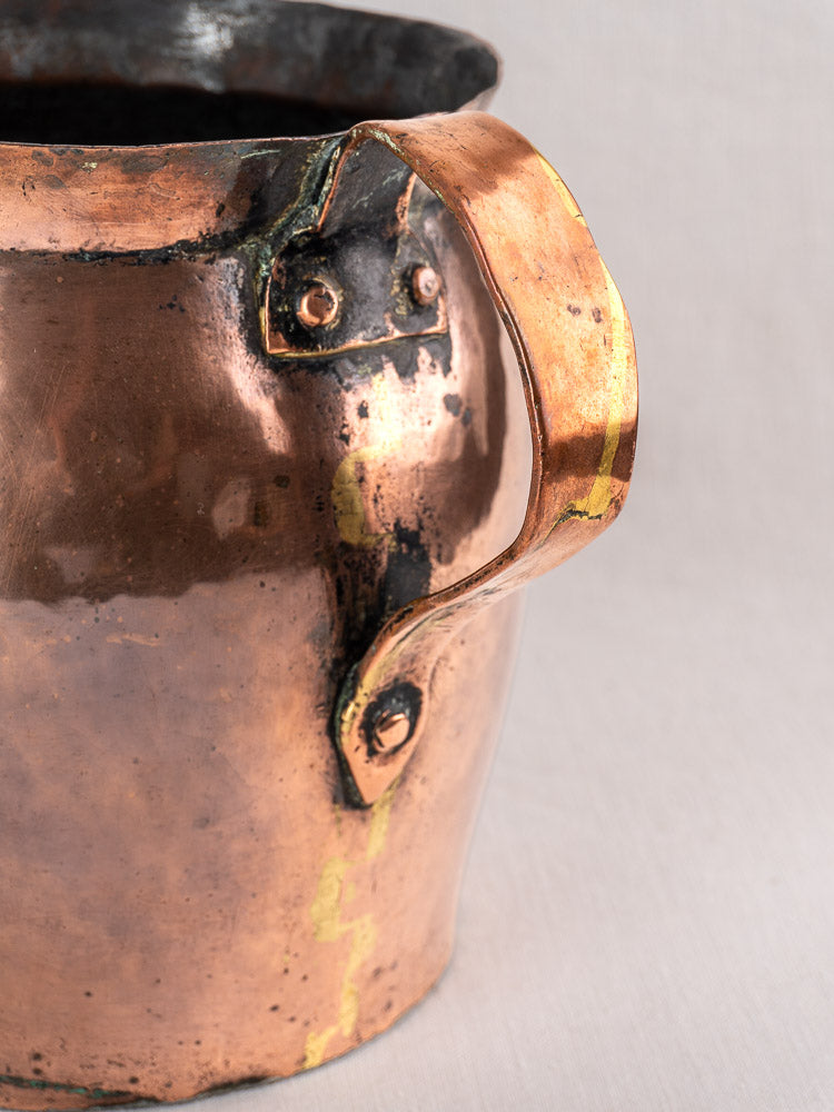 Antique French hammered copper pitcher with curved riveted handle and aged patina on a light background.
