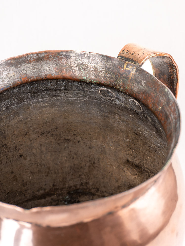 Late 18th century French copper pitcher, hammered finish, single handle, patina and wear, on light background.