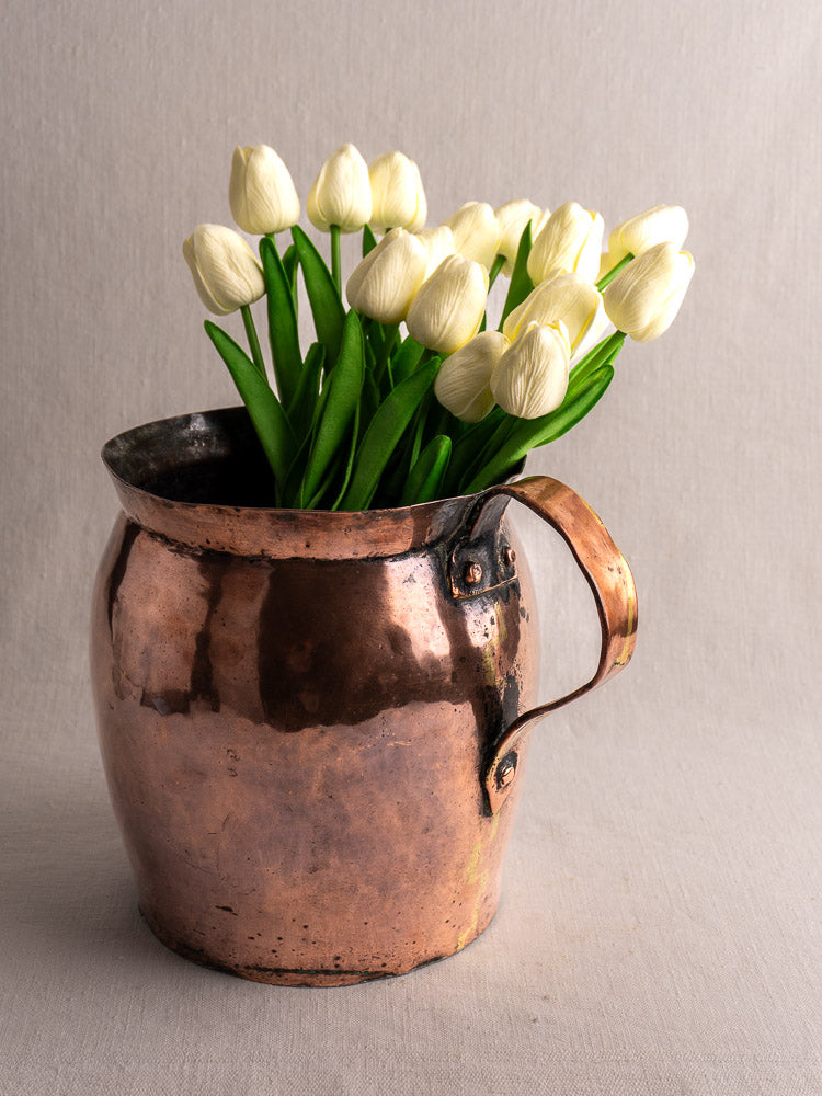 Antique French hammered copper pitcher, late 18th century, with white tulips, plain light background.