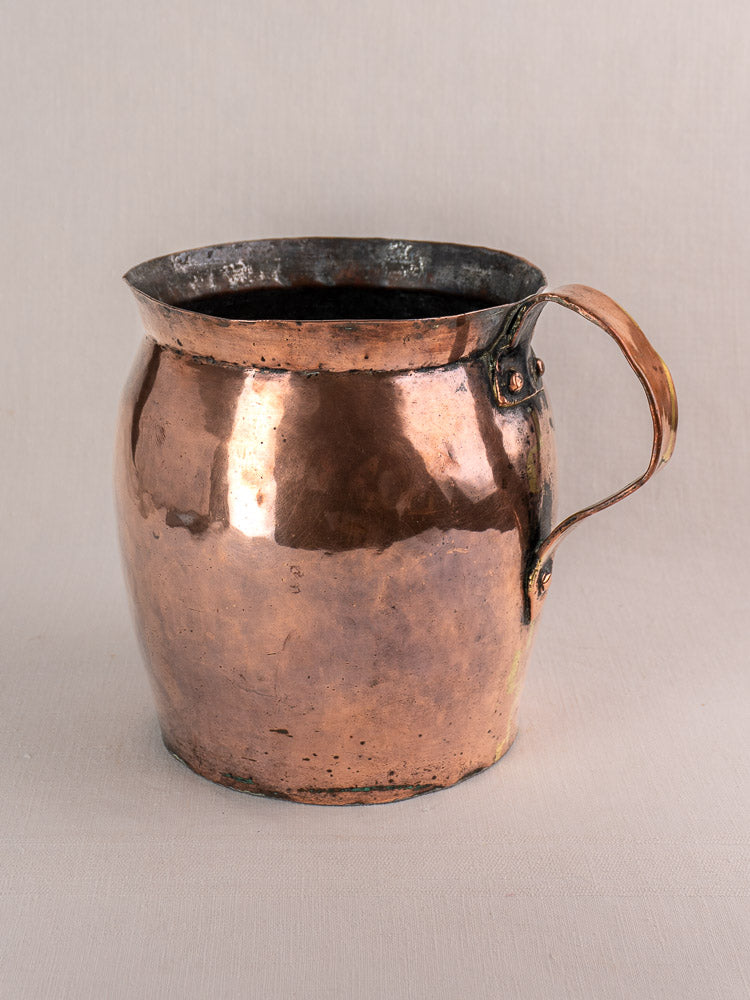 Late 18th century French hammered copper pitcher with rounded body, wide spout, and patinated curved handle on neutral surface.