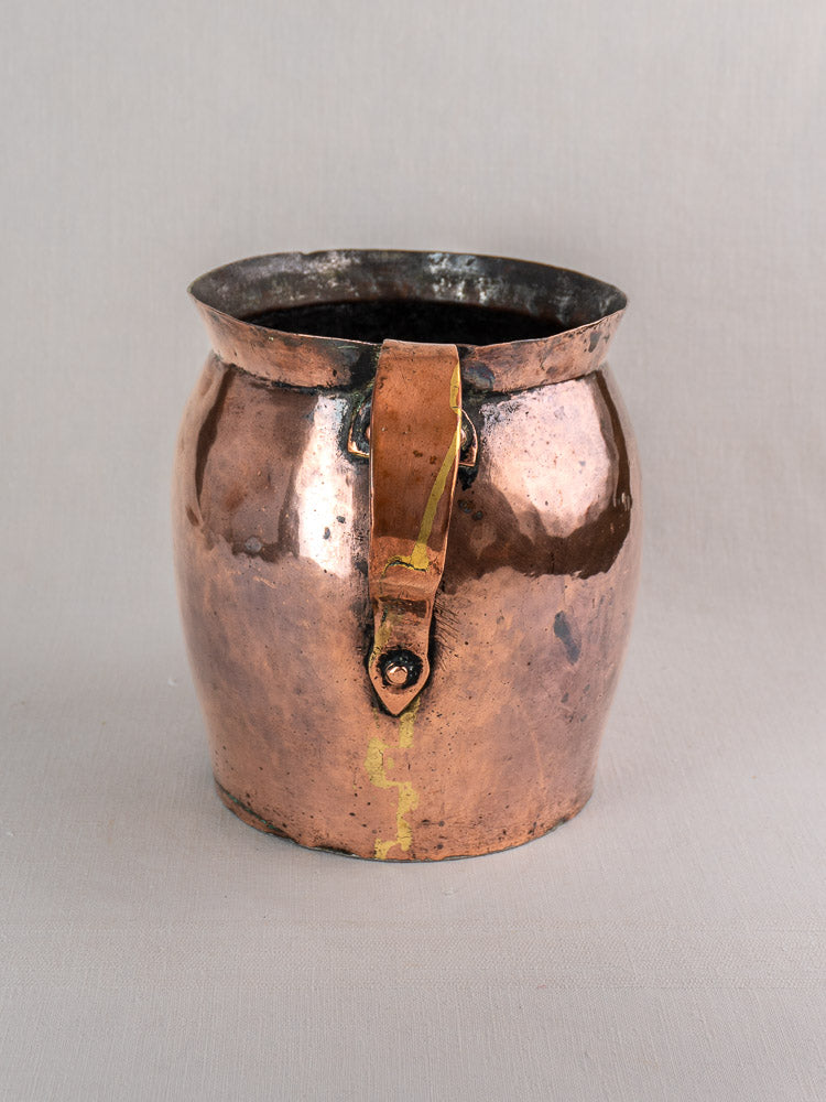 Antique French copper pitcher, late 18th century, hand-hammered with single handle and yellow solder repair on gray background.