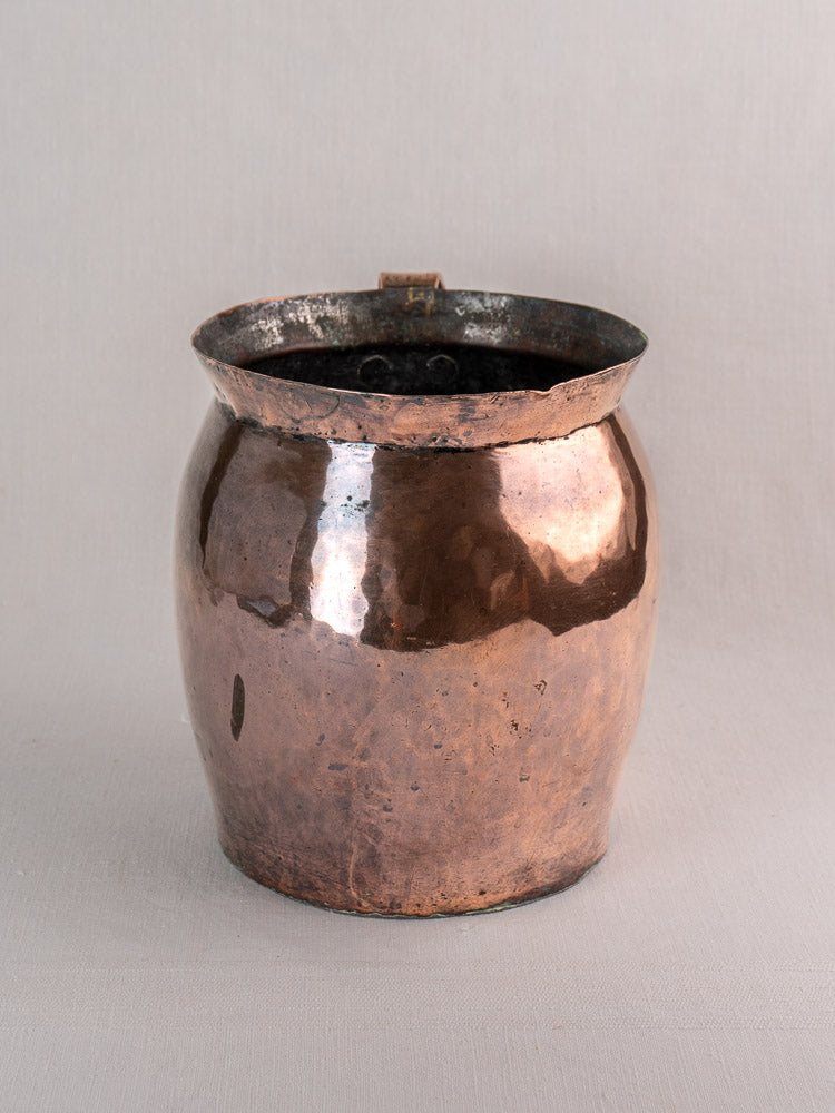 Antique late 18th-century French hammered copper pitcher with wide opening and rounded sides on neutral fabric.