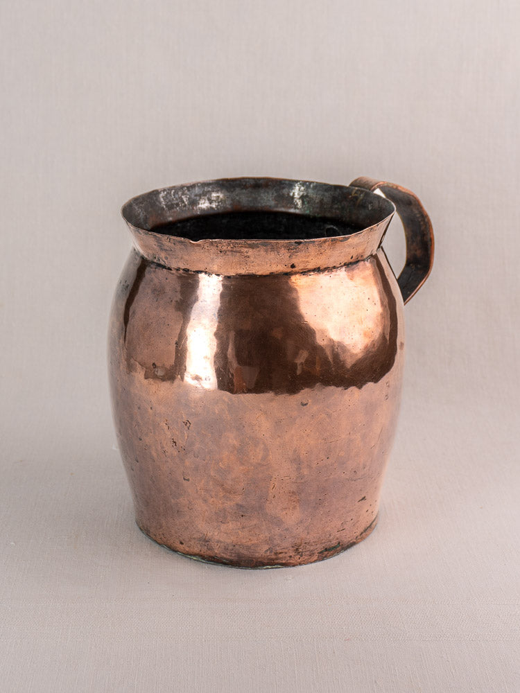 Antique French copper pitcher, late 18th century, hand-hammered with wide mouth and curved handle, on light gray background.