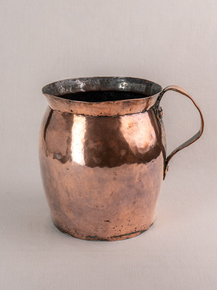 Late 18th-century French hammered copper pitcher with single curved handle and aged patina on light background.