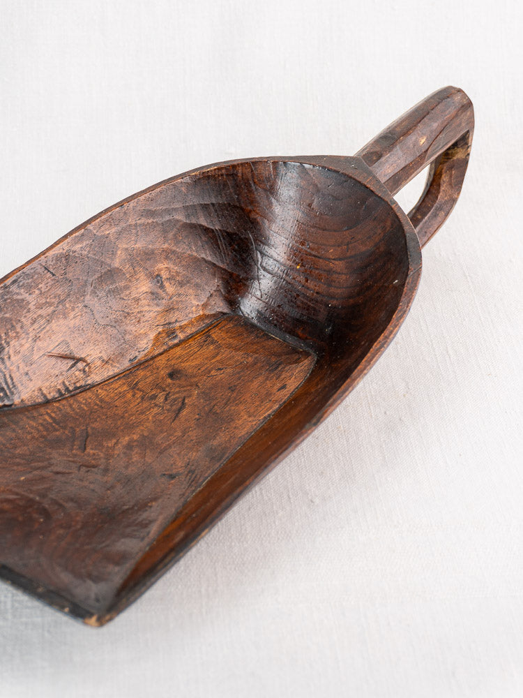 Antique French wooden grain scoop, 19th century, hand-carved with deep bowl and handle, set on light fabric.