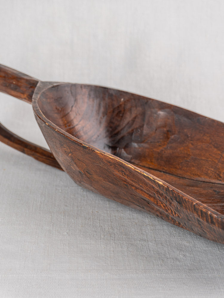 Antique French wooden grain scoop, 19th-century hand-carved, worn edges and wood grain, on light gray fabric background.