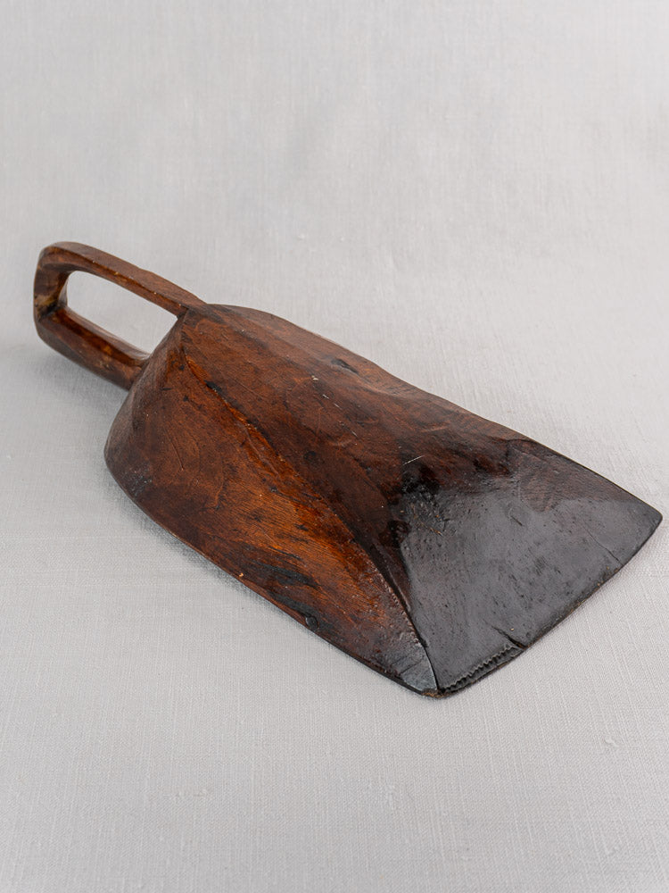 Antique French hand carved wooden grain scoop with dark finish, open handle, and worn details on light gray surface.