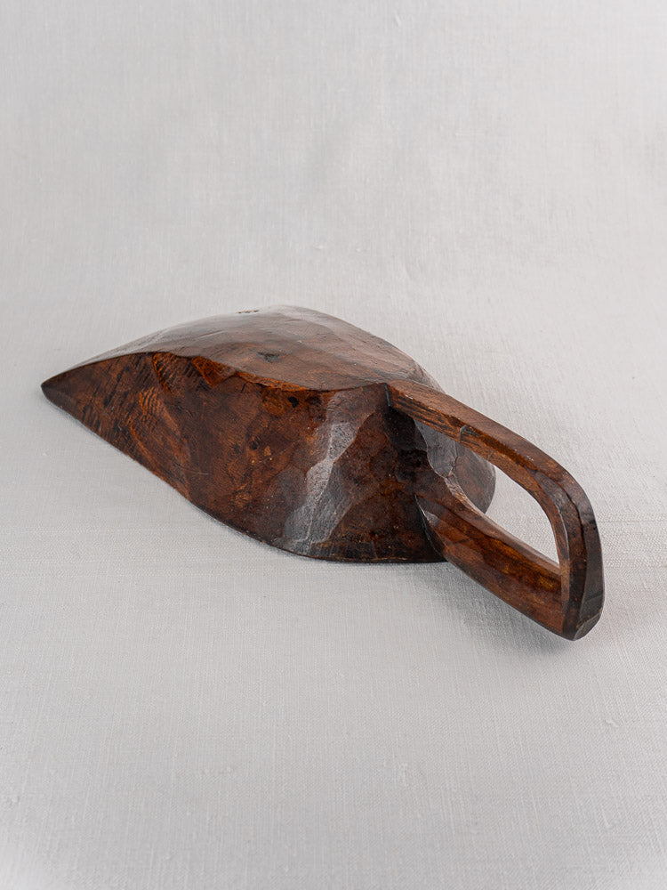 Antique French wooden grain scoop, hand carved with faceted dark wood and large handle on light gray fabric.