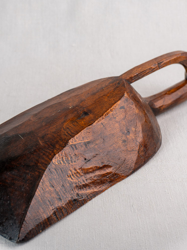 Antique French hand carved wooden grain scoop with curved handle and wood grain, on light fabric background. 19th century.