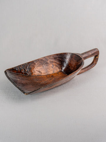 Antique French wooden grain scoop with wide, deep bowl and rich dark finish on light gray textured surface.