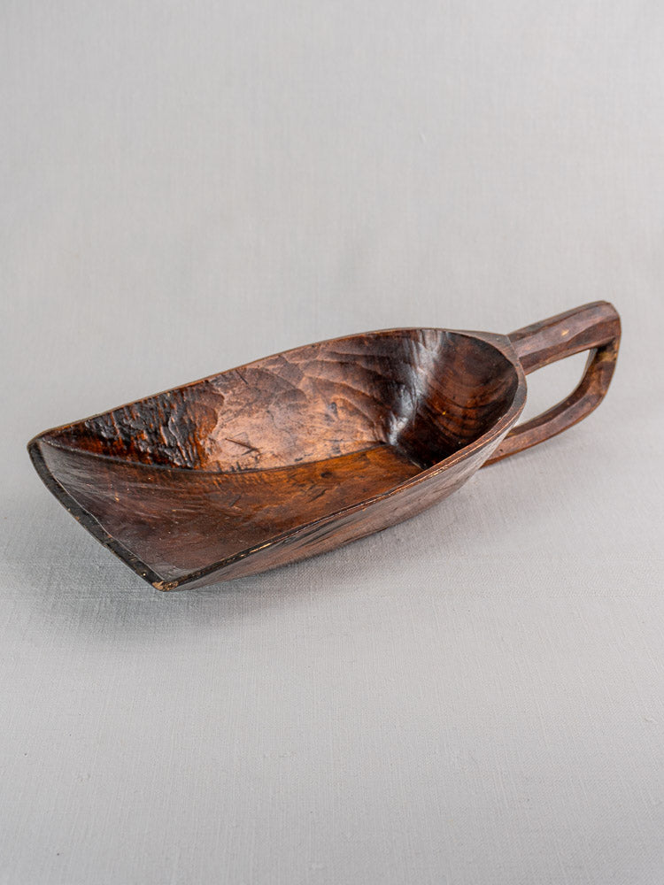 Antique French wooden grain scoop with wide, deep bowl and rich dark finish on light gray textured surface.