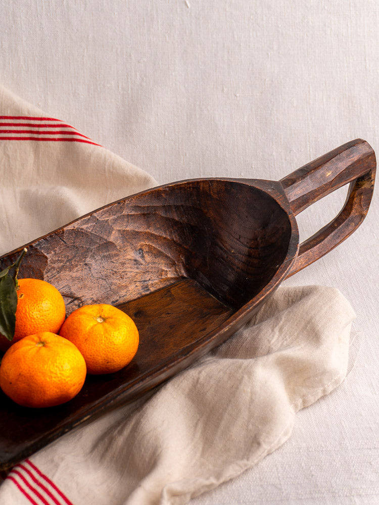 Antique French wooden grain scoop with three small oranges on cream cloth with red stripes, light fabric background.