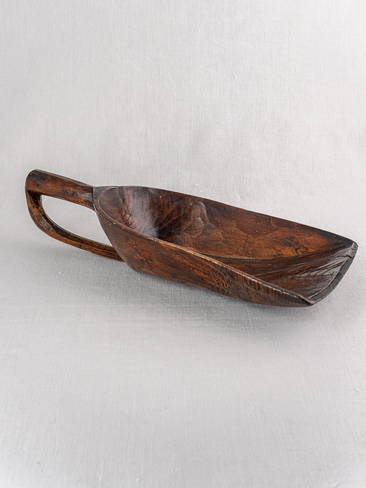 Antique French wooden grain scoop with hand-carved deep bowl and curved handle on a light textured surface.