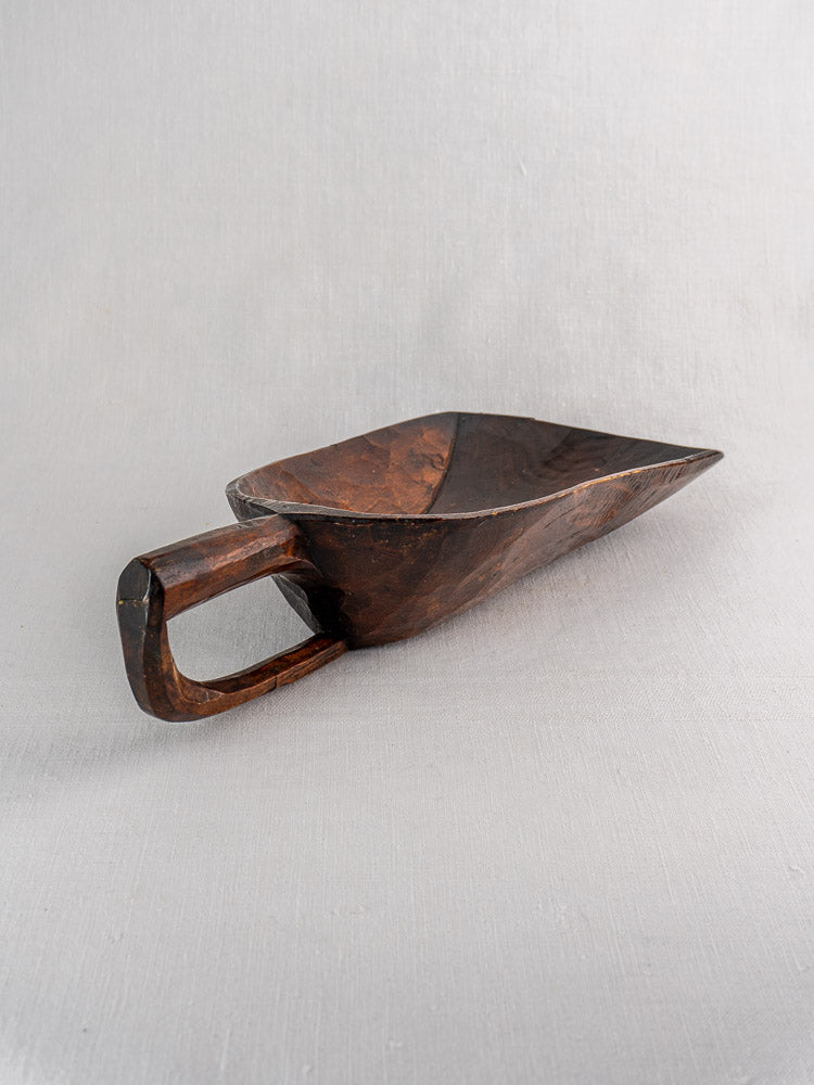 Antique French wooden grain scoop with deep, angular bowl and rectangular handle on light gray fabric.