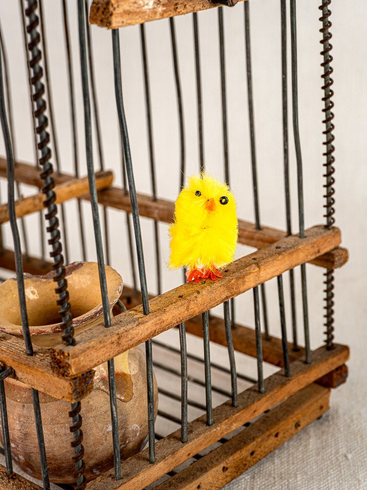 Antique French folk art wood and wire bird cage with toy chick, displayed beside a vintage ceramic pot.
