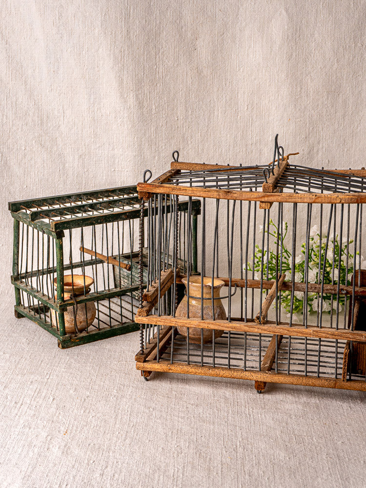 Pair of early 20th century French folk art wooden and wire bird cages with dishes; one holds a small green plant.