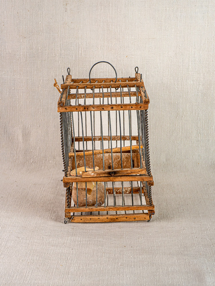 Antique French folk art wooden and wire bird cage with top handle, displayed on neutral fabric background.