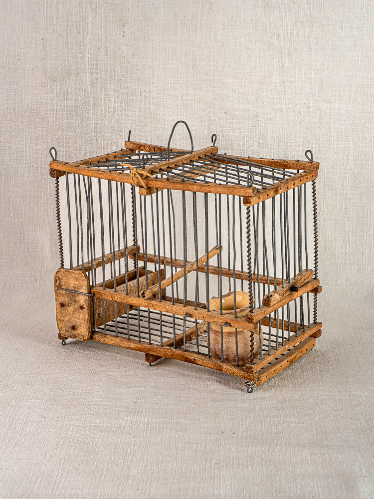 Antique French folk art bird cage, early 20th century wood and wire, on light textured fabric background.