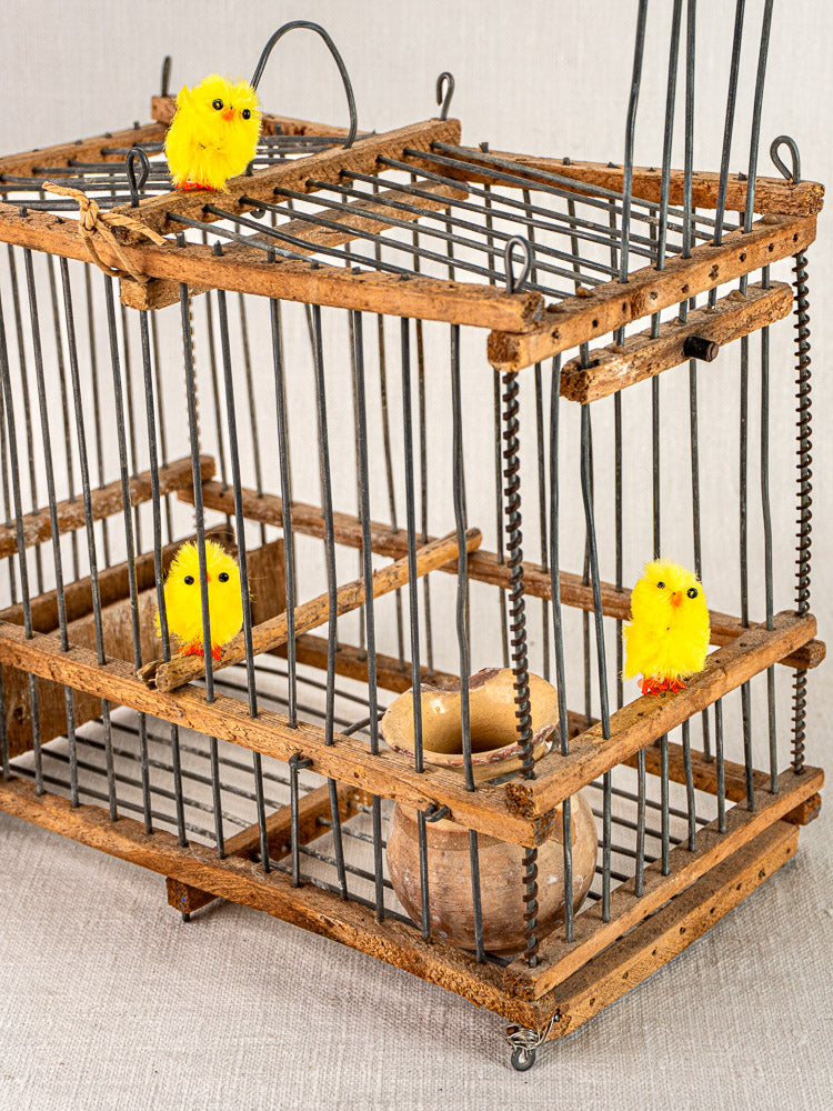 Antique French folk art bird cage in wood and wire with yellow toy chicks, brown eggshell bowl, on neutral fabric.