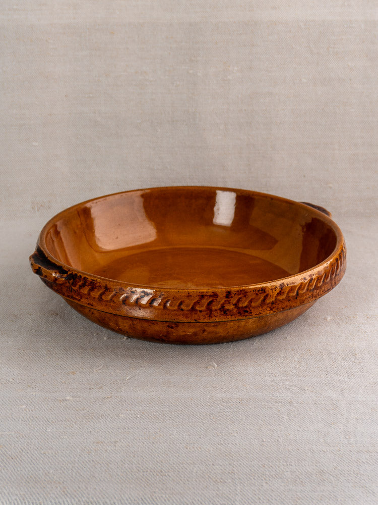 Antique French Vitry-le-François brown glazed stoneware gratin dish with classic decorative edge on neutral fabric.