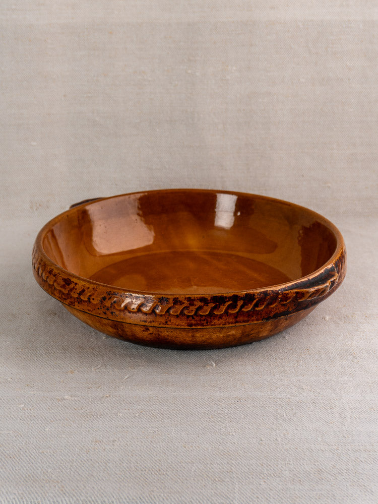 Antique French Vitry-le-François gratin dish in glossy brown stoneware with decorative rim on neutral fabric.