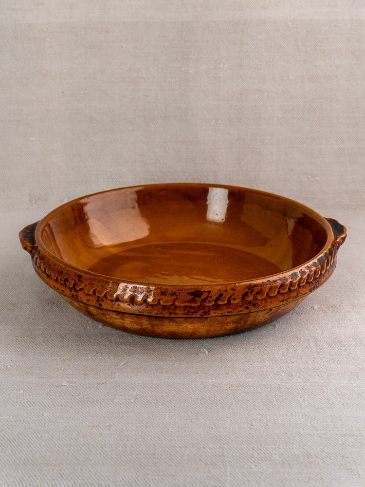Antique French Vitry-le-François brown stoneware gratin dish with side handles on neutral fabric.