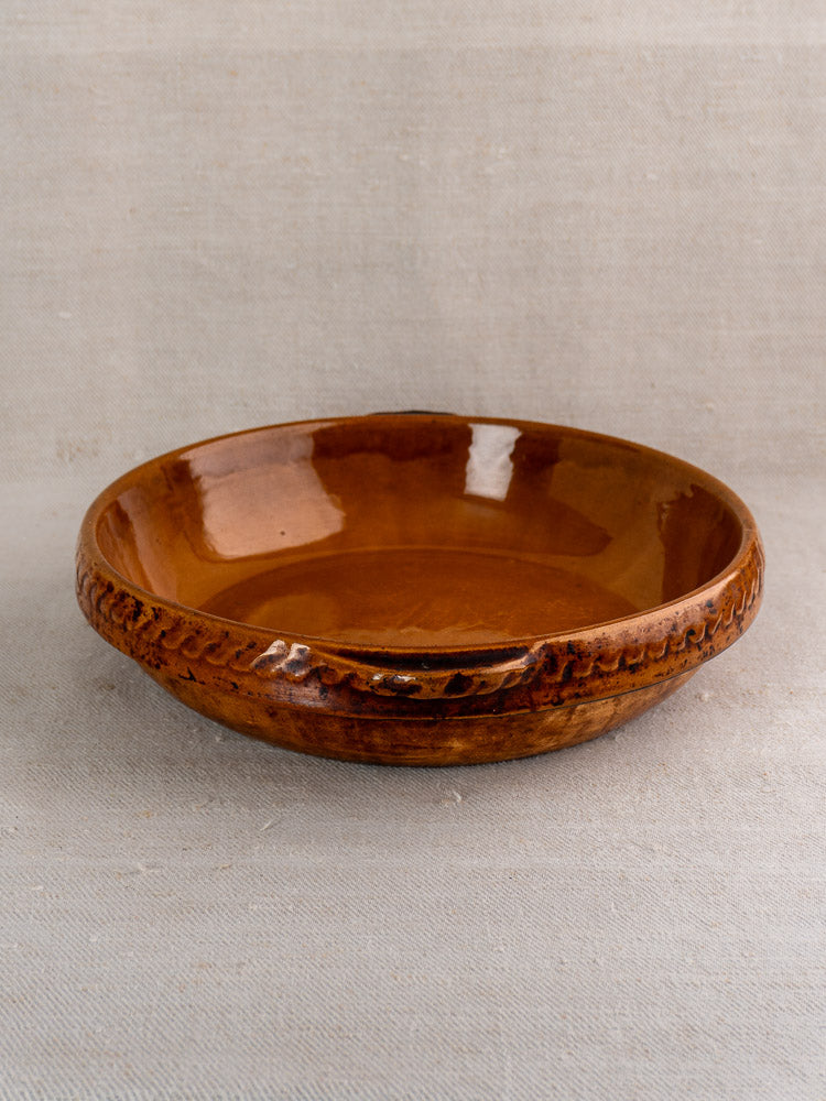 Antique French Vitry-le-François stoneware gratin dish with textured rim and rich brown glaze on beige fabric.
