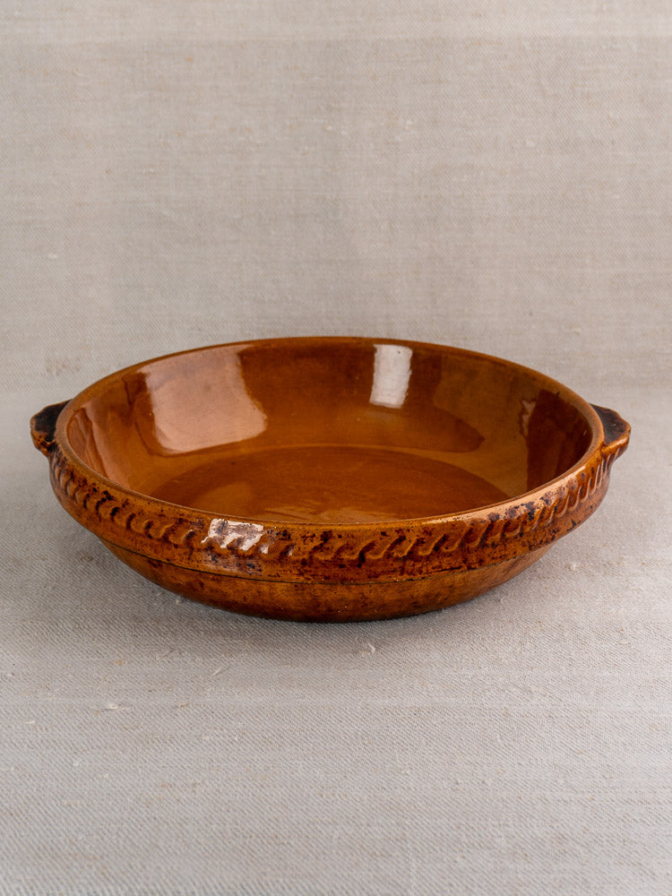 Antique French Vitry-le-François glazed stoneware gratin dish with two handles on neutral fabric.