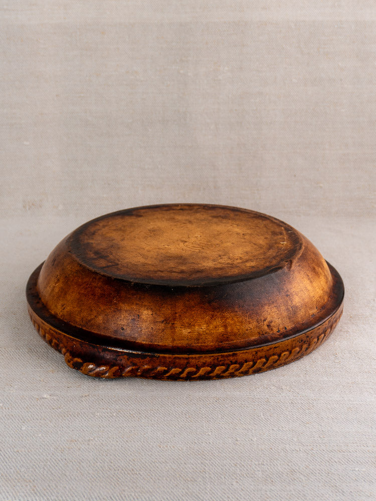 Antique French Vitry-le-François gratin dish in glazed stoneware with dark rustic finish, upside down on beige fabric.
