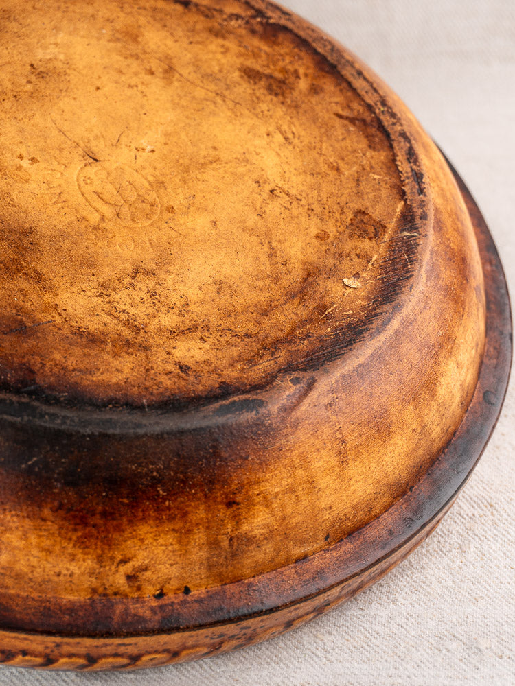Worn, brown, and lightly charred base of antique French Vitry-le-François gratin dish on textured fabric.