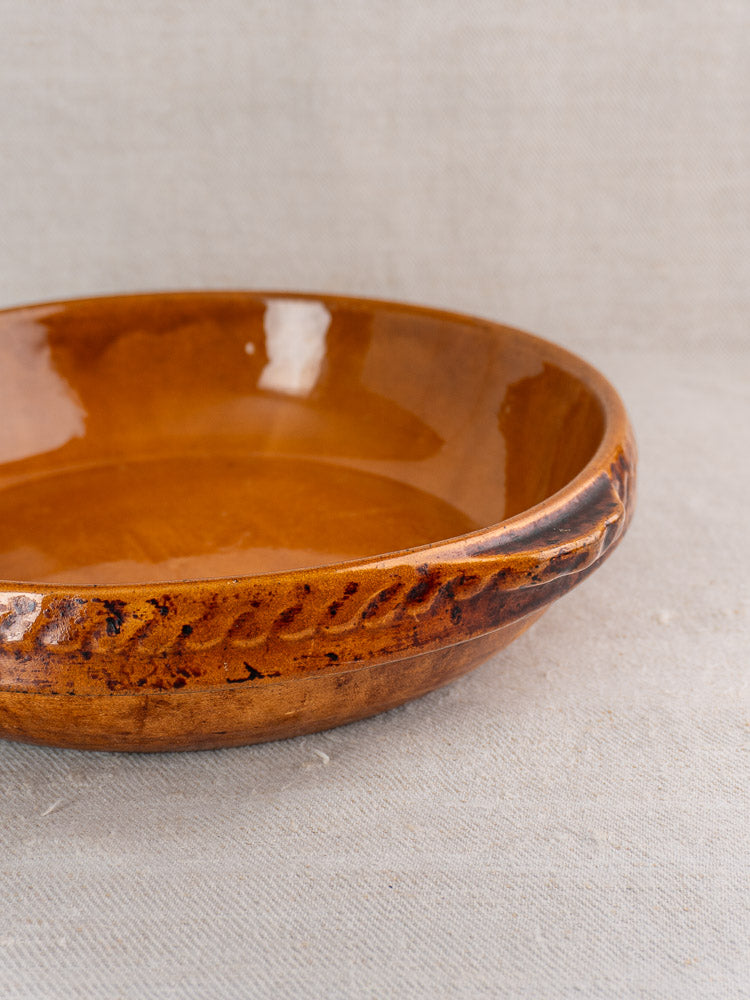 Antique French Vitry-le-François stoneware gratin dish with textured rim and rich brown glaze on light fabric.