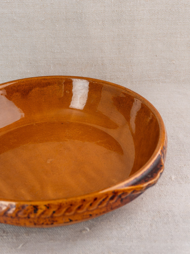 Antique French Vitry-le-François stoneware gratin dish with glossy brown glaze and textured rim on beige fabric.
