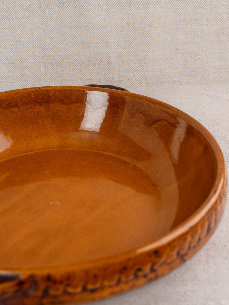 Antique French Vitry-le-François gratin dish, round glazed stoneware with handles, on neutral fabric background.
