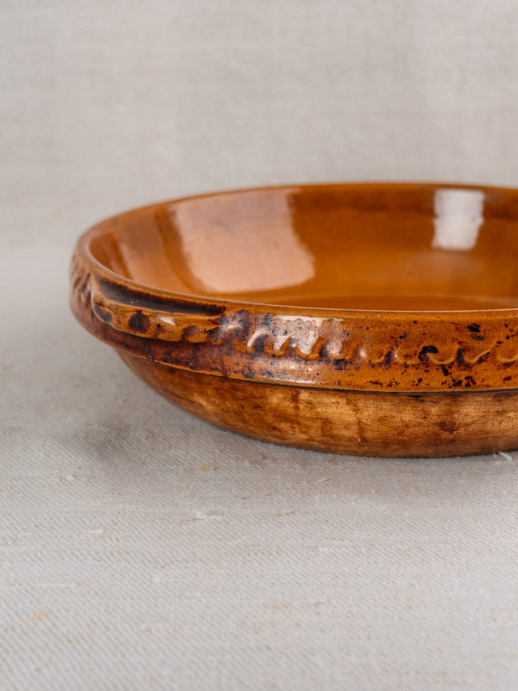 Antique French Vitry-le-François brown stoneware gratin dish with textured rim on light fabric surface.