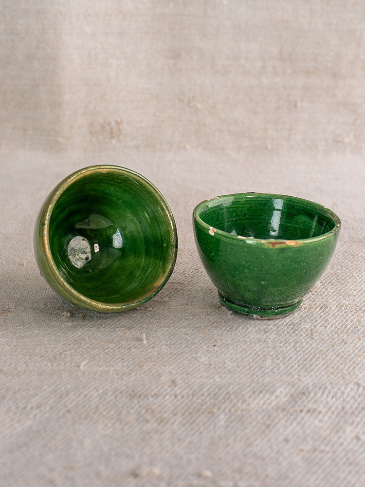 French green glazed ceramic bowls, upright and tipped, with glossy finish; Provençal Terre Vernissée pottery on beige fabric.