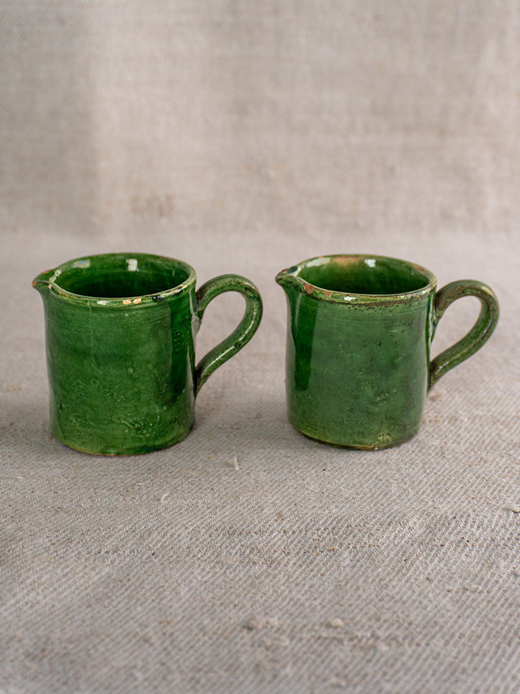 French green glazed pottery set with two small handled pitchers on textured beige fabric, classic Provençal country style.