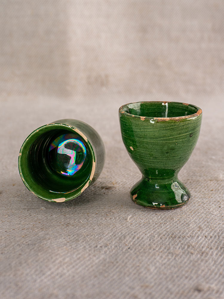 Set of eight Provençal green glazed ceramic egg cups, upright and on their sides atop textured fabric.